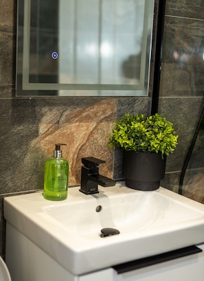 A bathroom sink with a green bottle, a black soap dispenser, and a potted plant. - Cosy Windsor Family Escape – Near LEGOLAND, Windsor Castle & London (Windsor)