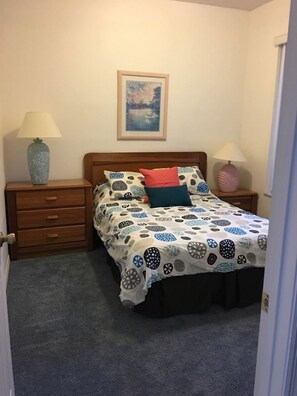 A bedroom with a bed, two nightstands, a lamp on each nightstand, a framed picture on the wall, and a carpeted floor. - Great Big, Beautiful Sunset Lakes Pool Home - SL001 (Kissimmee)