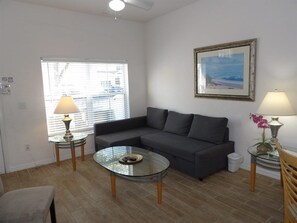 Una sala de estar con un sofá, una mesa de centro de vidrio, dos lámparas y un cuadro en la pared.