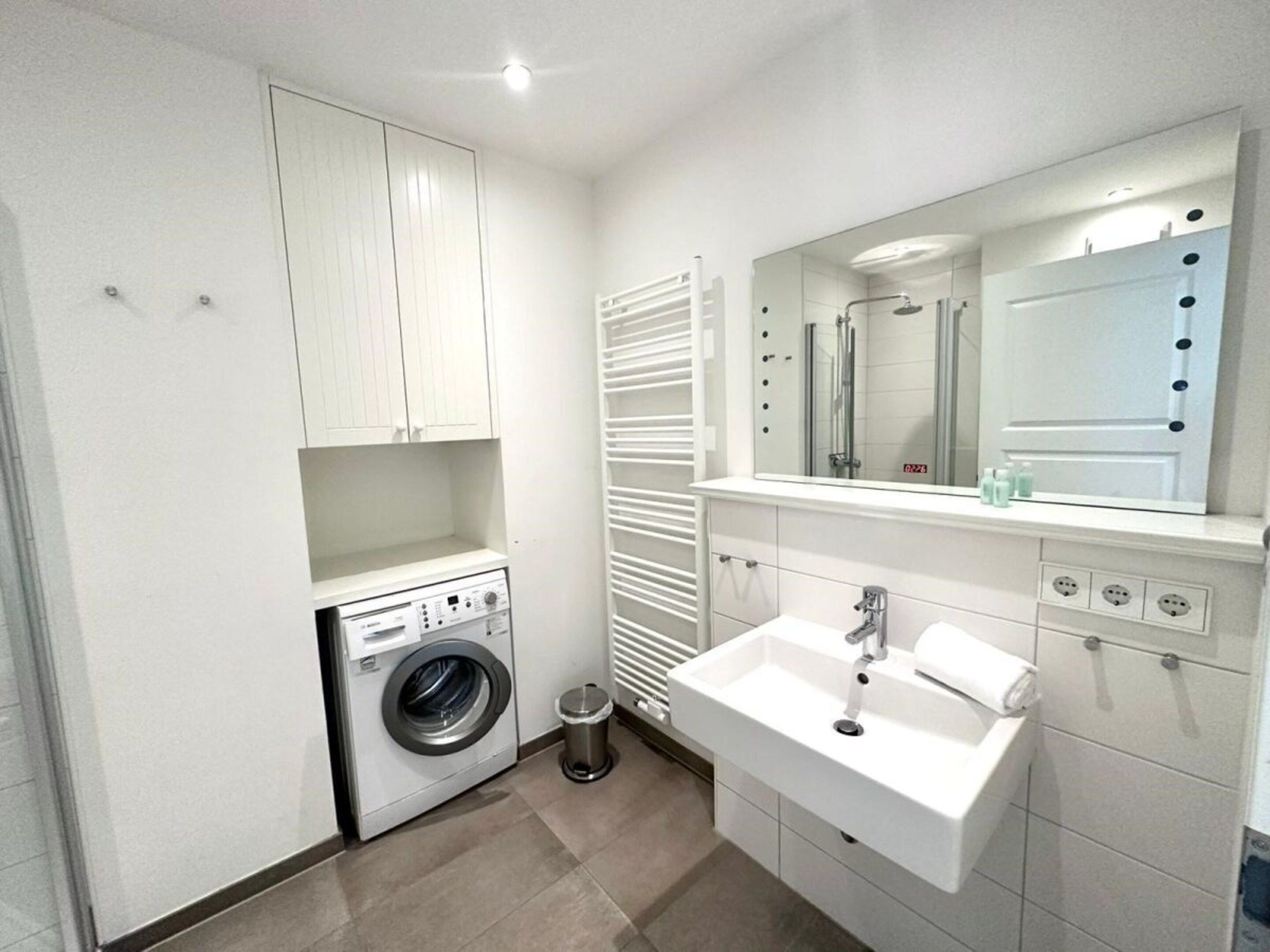 A compact bathroom with a built-in washing machine, a sink with a mirror, and a towel rack.