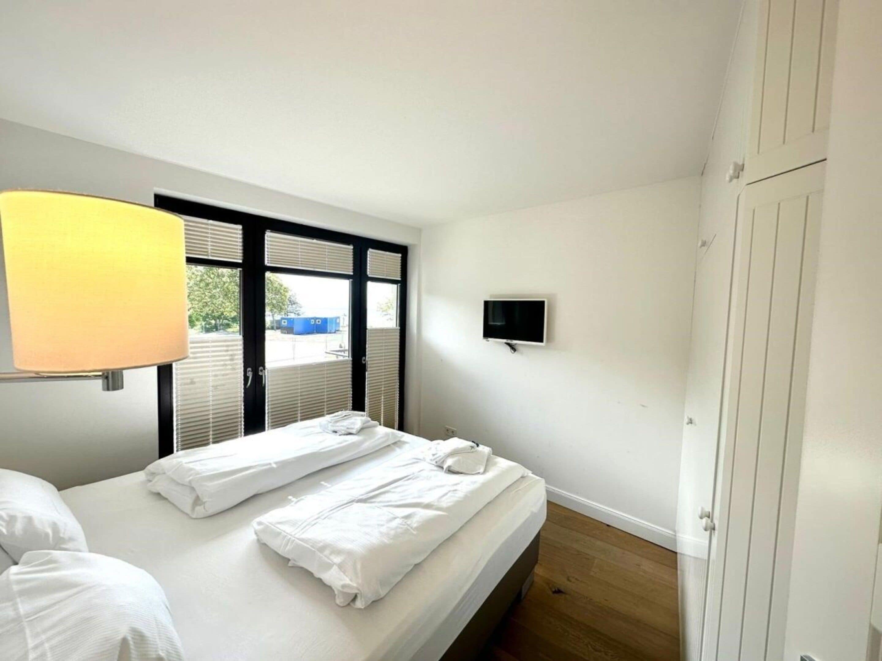 Una habitación de hotel con una cama, un televisor montado en la pared y una ventana con persianas.