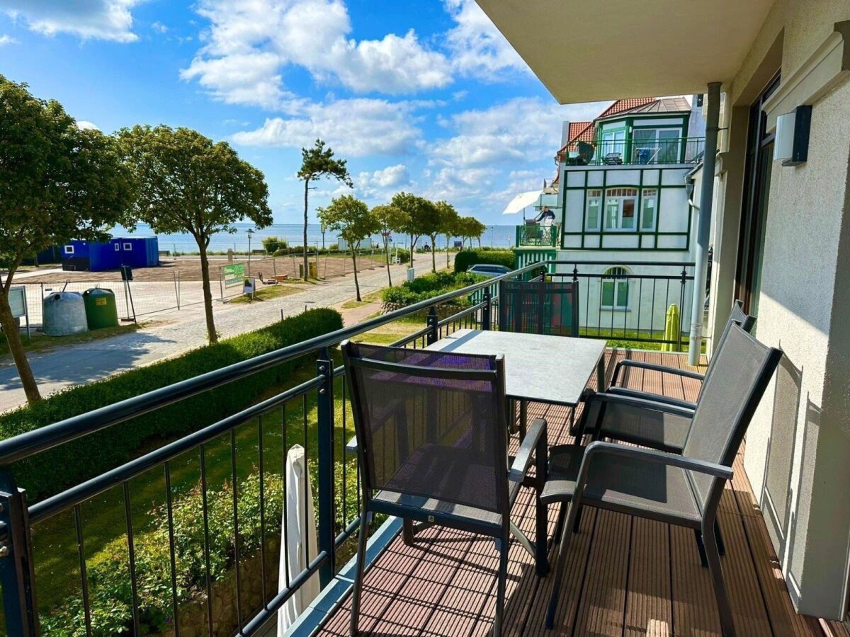 Un balcon agrémenté de mobilier d’extérieur, une vue sur un immeuble à la façade verdoyante et un ciel dégagé.