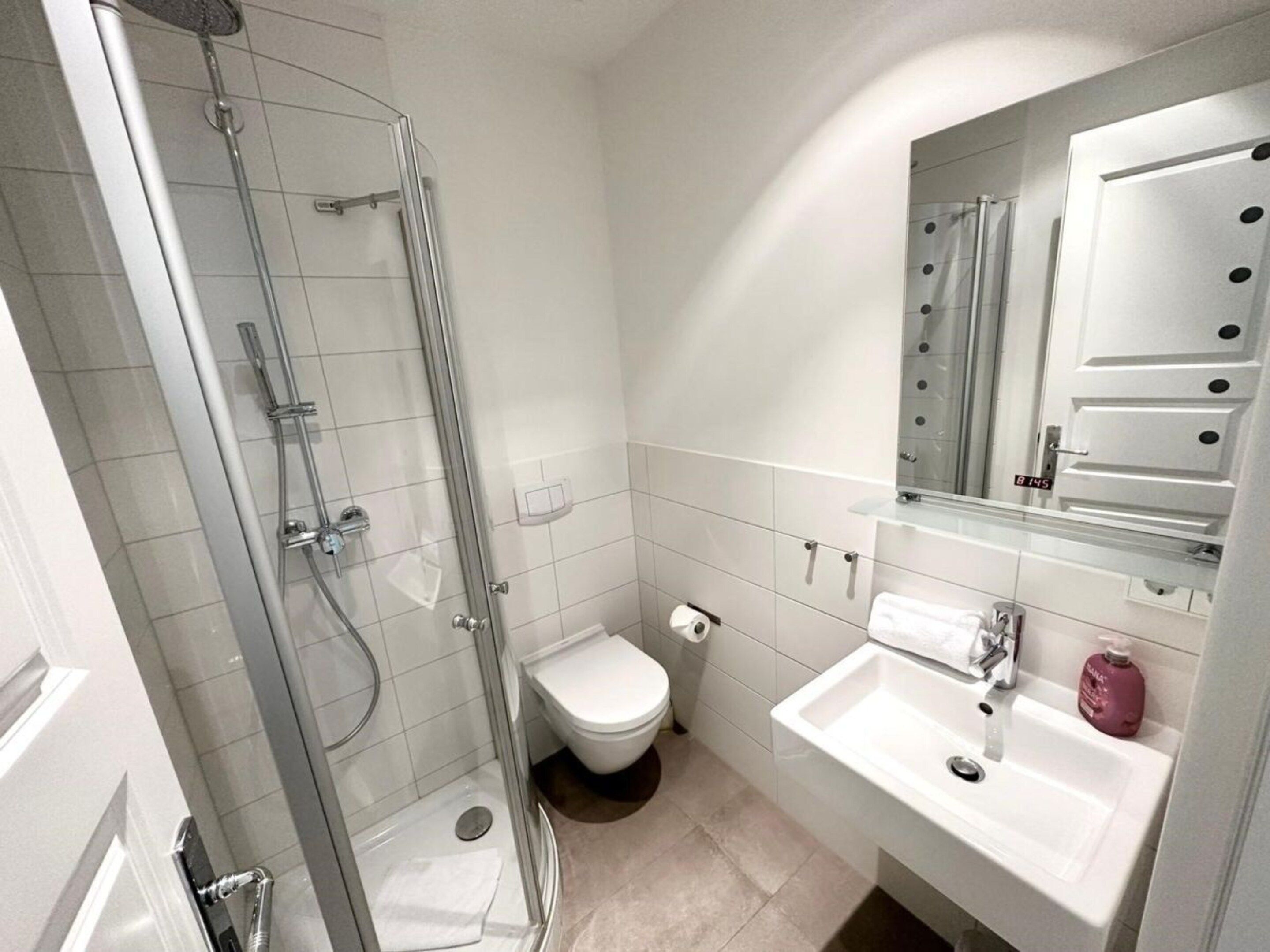 Un baño moderno con ducha envuelta en vidrio, inodoro, lavabo y espejo con tocador.