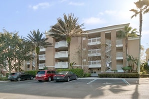 A multi-story building with balconies, a parking lot, and palm trees. - Luxurious Reunion Three Bed, Three Bath - SR001 (Four Corners)