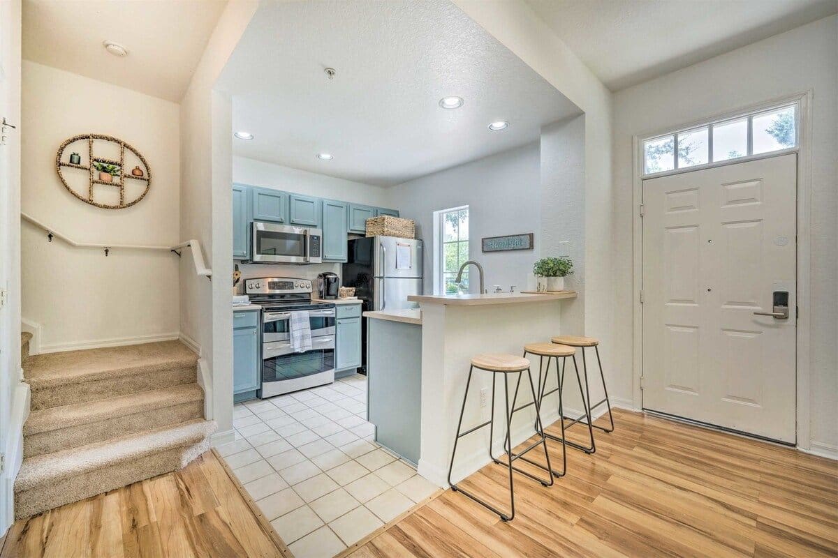 Una cocina moderna con armarios azul claro, una isla central y una escalera de madera.