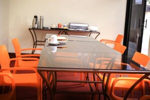 Un salón de conferencias con mesa de vidrio, sillas color naranja y una estación de café.