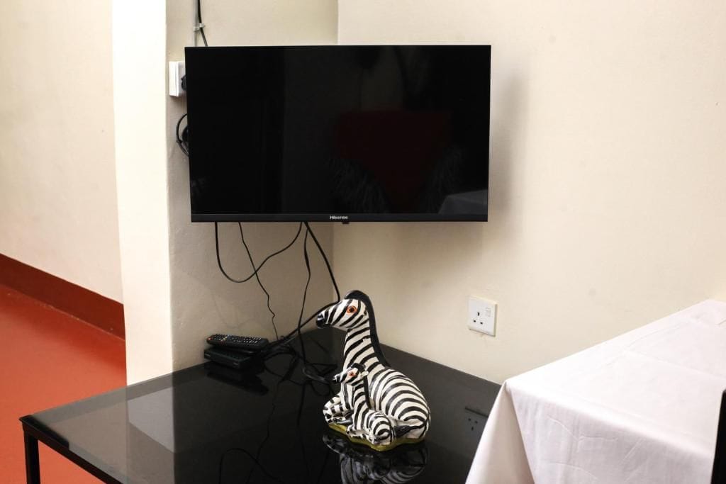 A flat-screen TV mounted on a wall, a zebra figurine on a table, and a white tablecloth on a table.