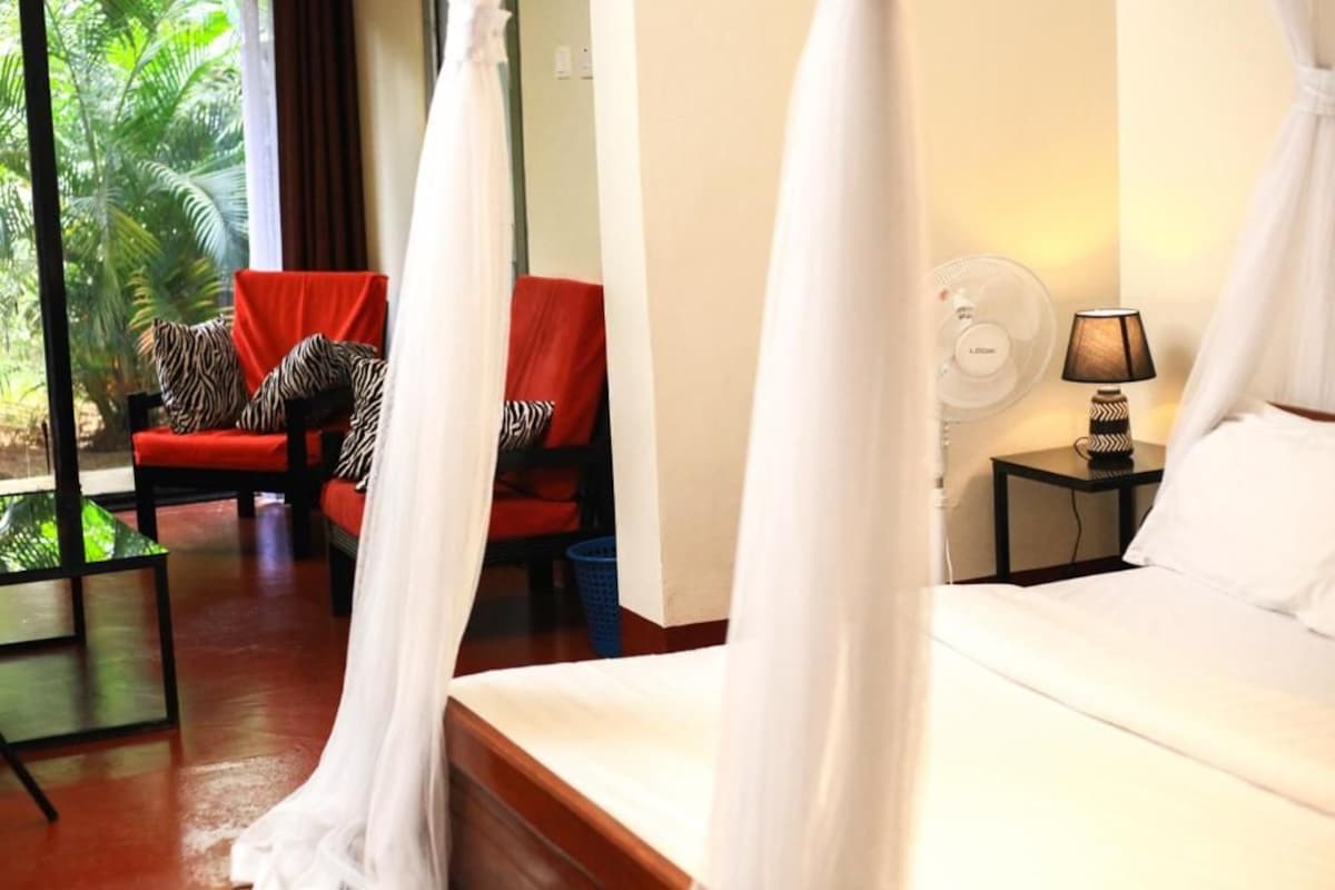 Habitación de hotel con cama, una silla con cojines de estampado de cebra, una mesita de noche con lámpara y vistas a zonas verdes.