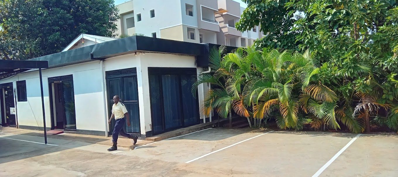 A building with a modern design, featuring a flat roof and large windows. There is a parking area in front of the building, and a person is walking towards the entrance.