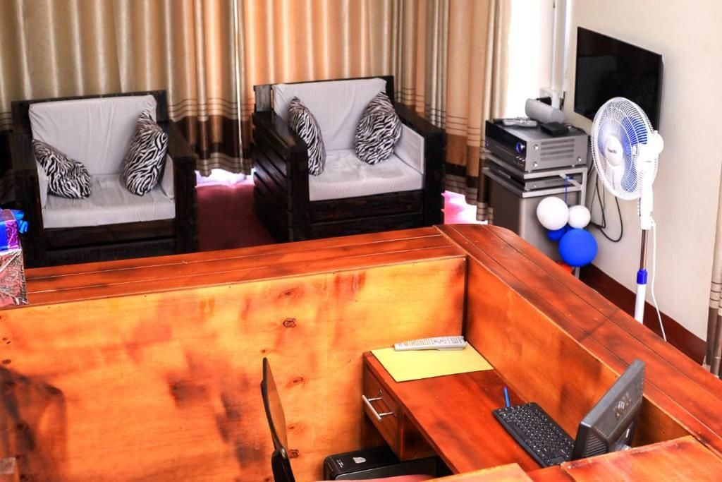 Una habitación de hotel con dos sofás de madera, un escritorio con computadora, un ventilador y un televisor.