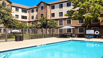Une piscine avec un panneau indiquant qu’il est interdit de plonger, un panneau d’avertissement concernant la présence d’un sauveteur, et un patio clôturé avec des meubles d’extérieur.