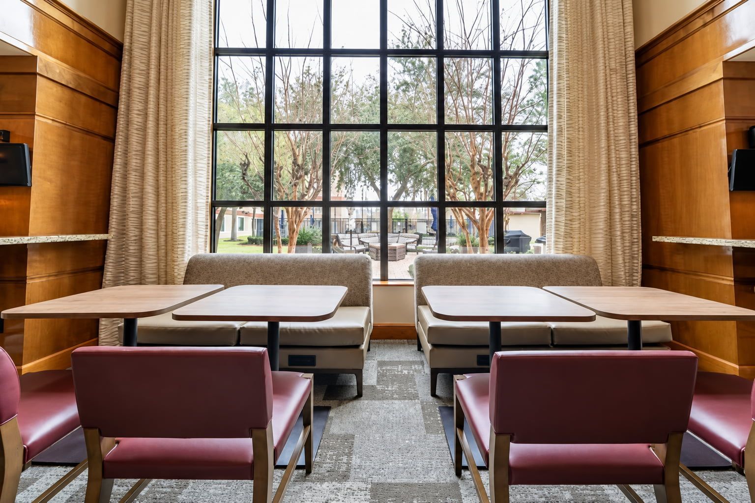 Un comedor con asientos tipo cabina y mesas, ventanas grandes con cortinas y vistas al exterior.