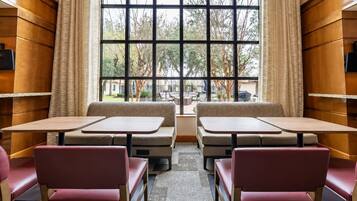 Un comedor con asientos tipo cabina y mesas, ventanas grandes con cortinas y vistas al exterior.