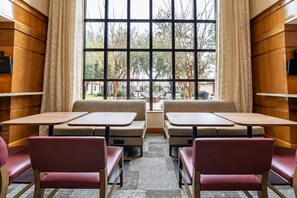 Un comedor con asientos tipo cabina y mesas, ventanas grandes con cortinas y vistas al exterior.