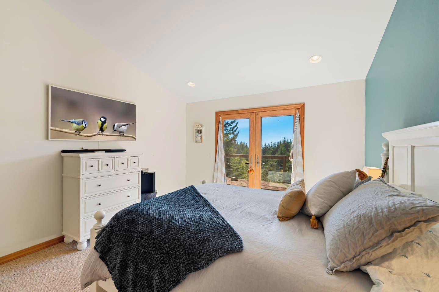 Ein Schlafzimmer mit einem Bett, einem Schminktisch, einem Vogelgemälde und einer Glastür zum Balkon.