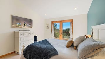 Ein Schlafzimmer mit einem Bett, einem Schminktisch, einem Vogelgemälde und einer Glastür zum Balkon.
