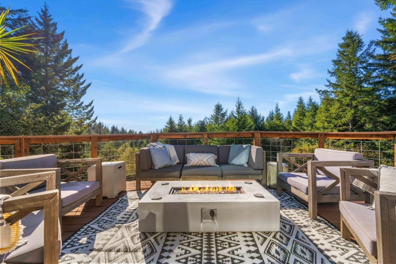 An outdoor deck with a fire pit, seating area, and a view of a forest.