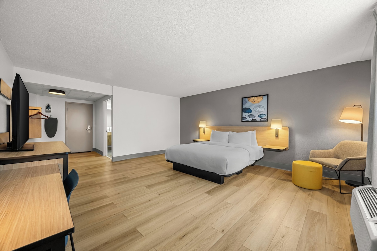 Ett modernt hotellrum med en säng, sängbord, ett skrivbord, en stol och en soffa.