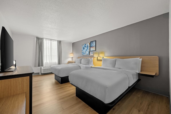 Ett hotellrum med två sängar, ett skrivbord, en TV och ett fönster med gardiner.