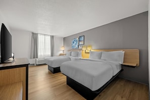 Ett hotellrum med två sängar, ett skrivbord, en TV och ett fönster med gardiner.