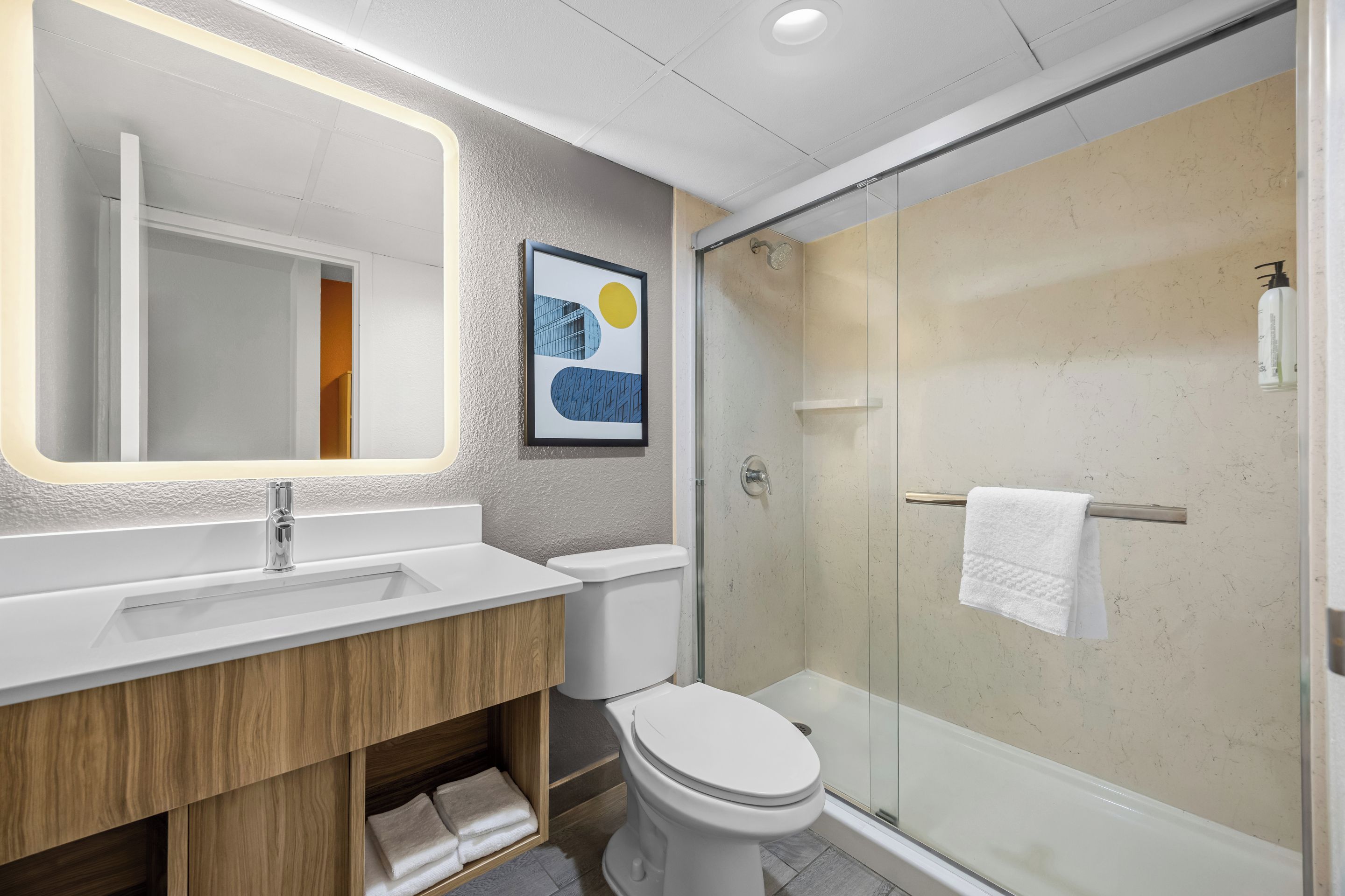 Un baño moderno con ducha de vidrio, inodoro blanco y lavamanos con mueble de madera.