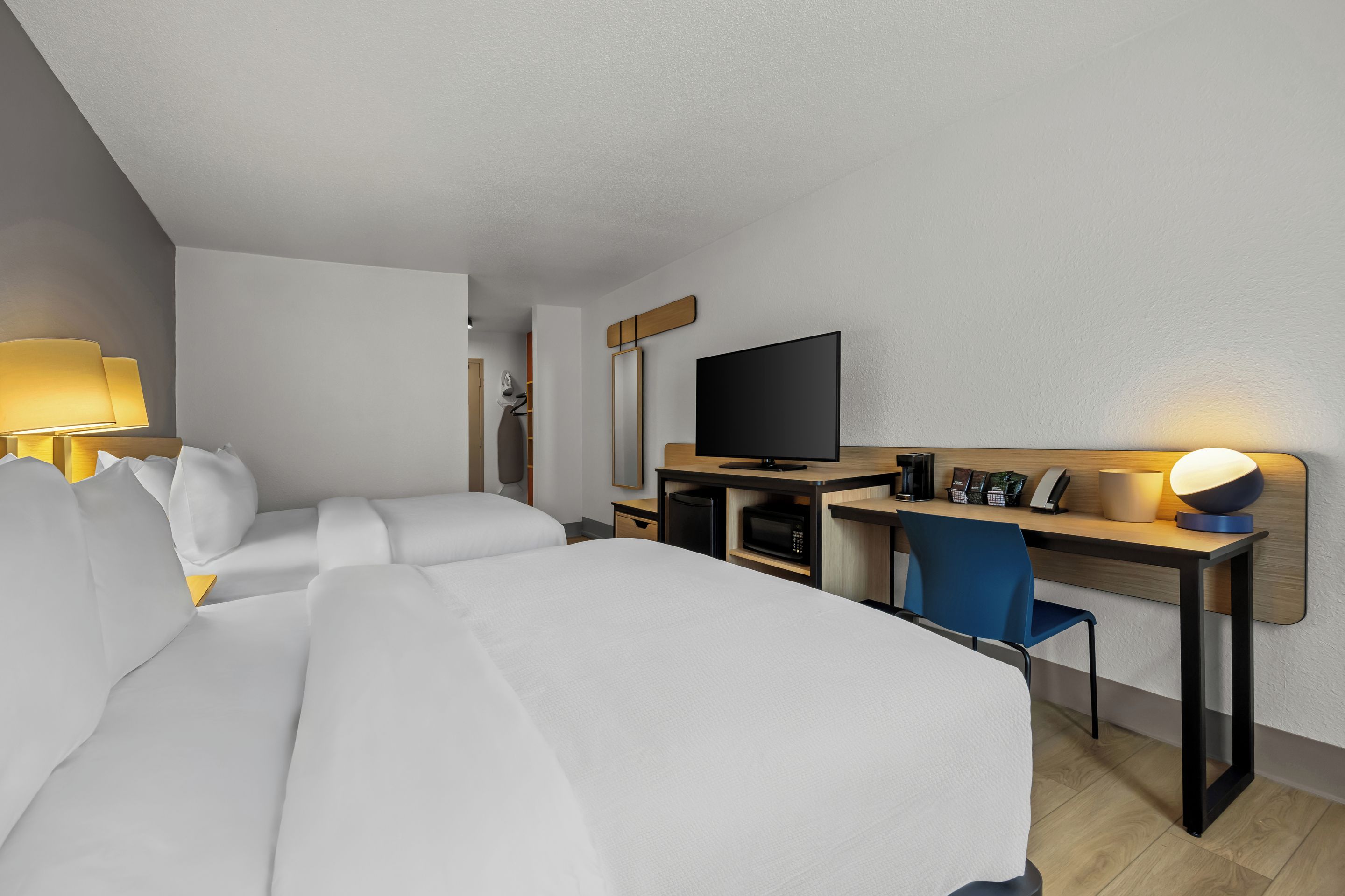A hotel room with a bed, desk, chair, TV, and a lamp.