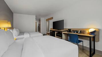 A hotel room with a bed, desk, chair, TV, and a lamp.
