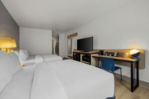 Habitación de hotel con cama, escritorio, silla, televisor y lámpara.