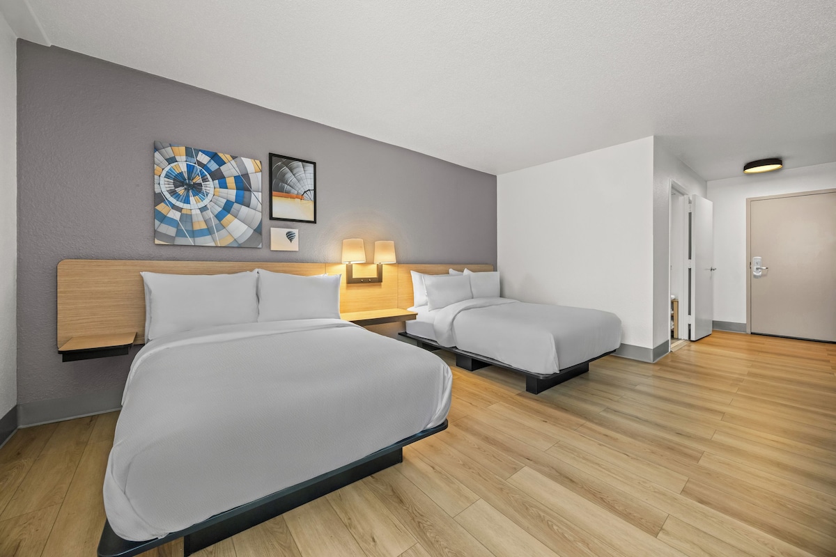 Ett hotellrum med två sängar, en sänggavel i trä, en vägglampa och en dörr.
