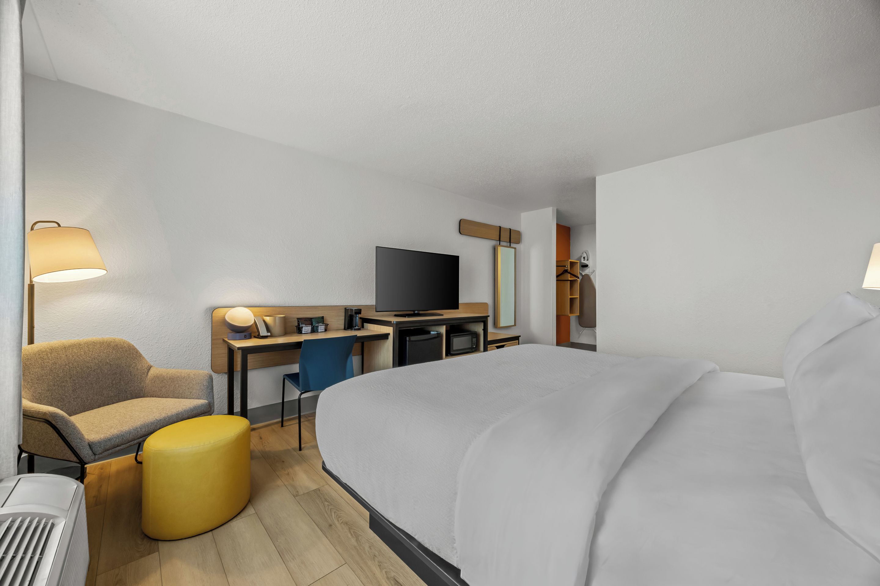 A hotel room with a bed, a desk, a chair, a television, and a lamp.