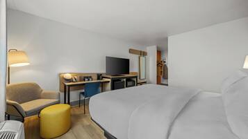 A hotel room with a bed, a desk, a chair, a television, and a lamp.
