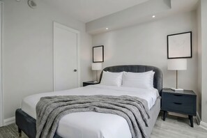 A neatly made bed with a grey blanket, two bedside tables with lamps, and framed artwork on the walls. - Deluxe Living in Yorkville Stylish 2-BR Condo (Toronto)