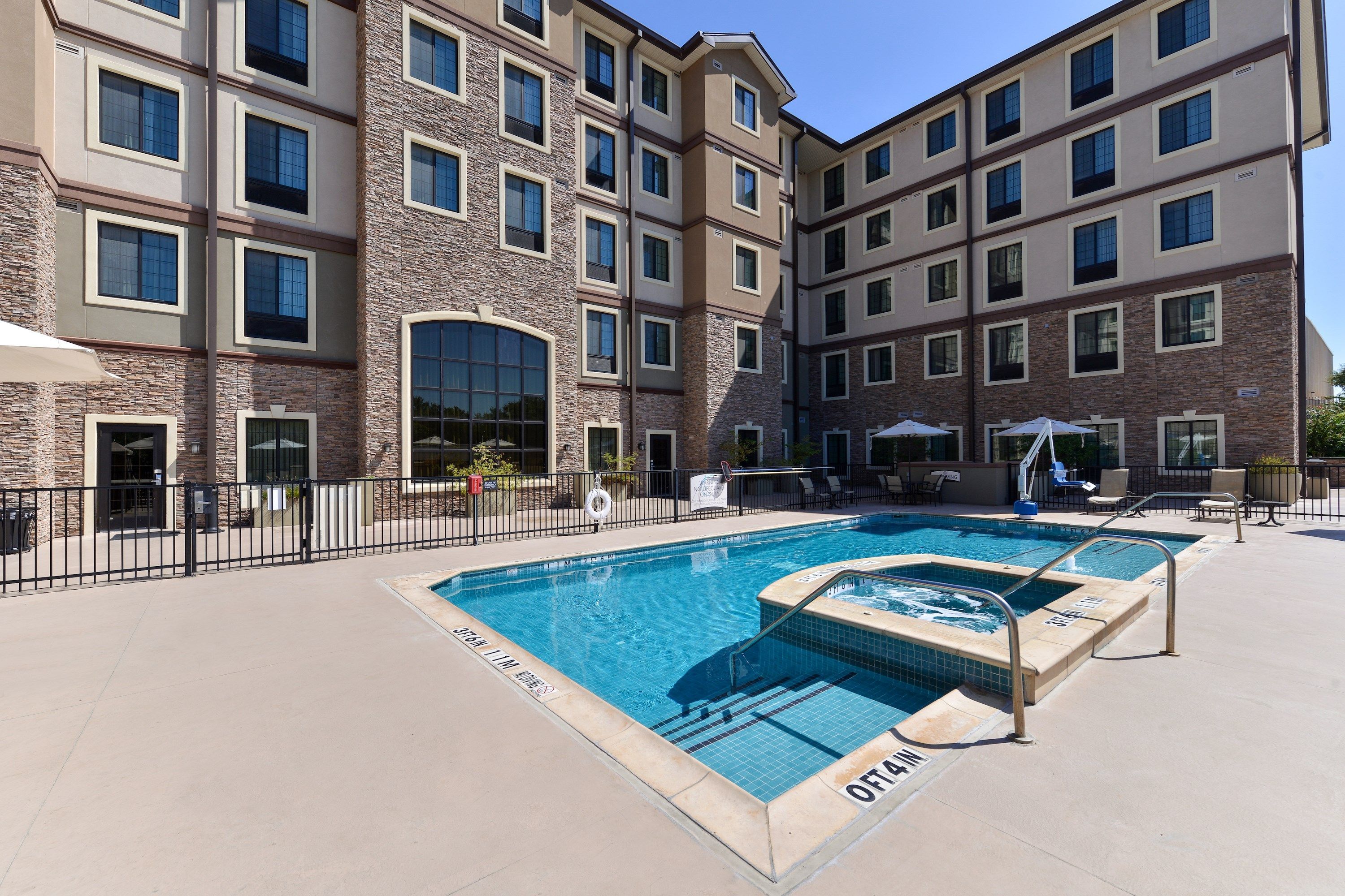 A multi-story hotel with a swimming pool area, outdoor seating, and a covered patio.