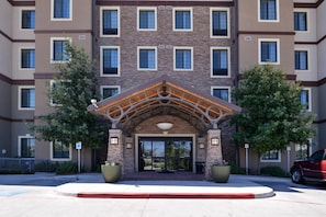 A multi-story building with a central entrance featuring a wooden archway and large potted plants on either side. - Accessible 2BR Suite w/ Daily Hot Breakfast + Pool (San Antonio)
