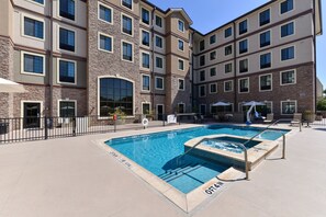 Ein mehrstöckiges Hotel mit Poolbereich, Außenbereich zum Sitzen und einer überdachten Terrasse.