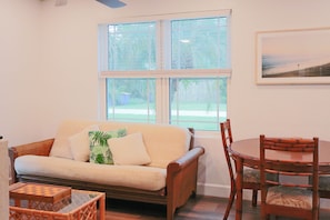 Ein Wohnzimmer mit einer Couch, einem Esstisch mit Stühlen, einem Fenster mit Jalousien und einem gerahmten Bild an der Wand.