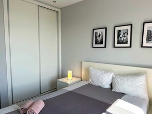 Ein Hotelzimmer mit einem Bett, einem Nachttisch mit Lampe, einem Kleiderschrank und drei gerahmten Bildern an der Wand.