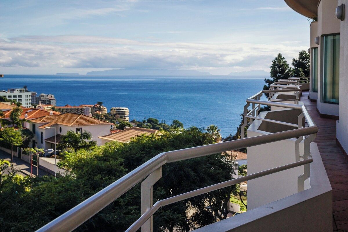 A balcony with a view of the sea and surrounding buildings.
