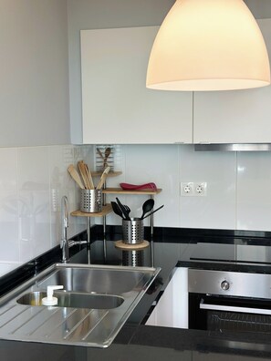 A modern kitchen with a stainless steel sink, a built-in oven, and a hanging light fixture. - Cozy Duplex Retreat by Green Parc & Ocean View (Funchal)