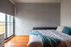 A bedroom with a large window, a bed with white bedding, and a grey wall. - Sky View - Spacious Stay with Pool & Gym (Funchal)