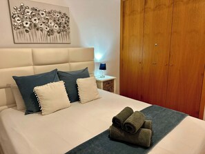 A neatly made bed with pillows, a folded towel, and a wall art piece above it.