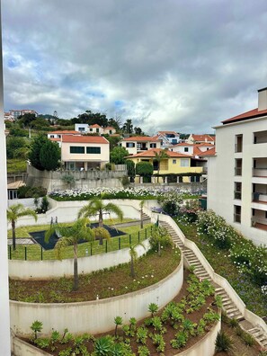 A residential area with houses, a curved pathway, and a small garden with plants and flowers. - Sea view - Peaceful Atlantic View by Cristo Rei (Caniço)