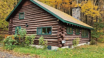 A log cabin with a stone chimney, surrounded by autumn foliage.