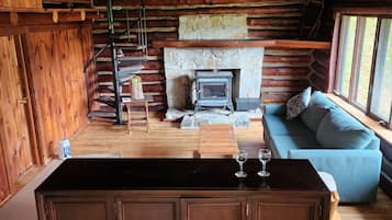 A log cabin interior with a stone fireplace, wooden furniture, and a staircase.