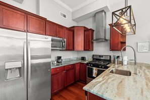 A kitchen with stainless steel appliances, wooden cabinets, a marble countertop, and a modern pendant light. - Trendy Urban Haven 1BD | Min to Old City | Fits 2 (Philadelphia)