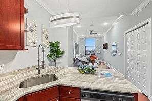 A modern kitchen with a marble countertop, a built-in dishwasher, and a view to the living area. - Charming NoLib Studio | Sleeps 2 | Onsite Fitness (Philadelphia)