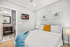 Ein Schlafzimmer mit Bett, Fernseher, Kunstwerken, einem Spiegel und einem durch eine offene Tür einsehbaren Badezimmer.