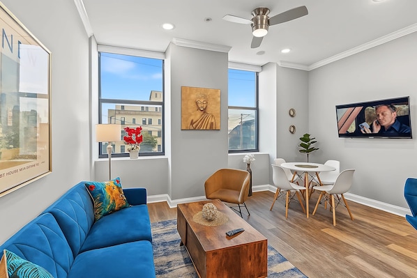 Un salon moderne avec un canapé bleu, une table basse en bois et un coin repas avec des chaises blanches.