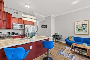 Una cocina moderna con armarios rojos, una isla central y una zona de comedor con un sofá azul y una mesa de centro.