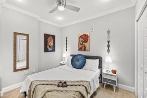 Un dormitorio con cama, mesitas de noche, ventilador de techo y obras de arte en las paredes.